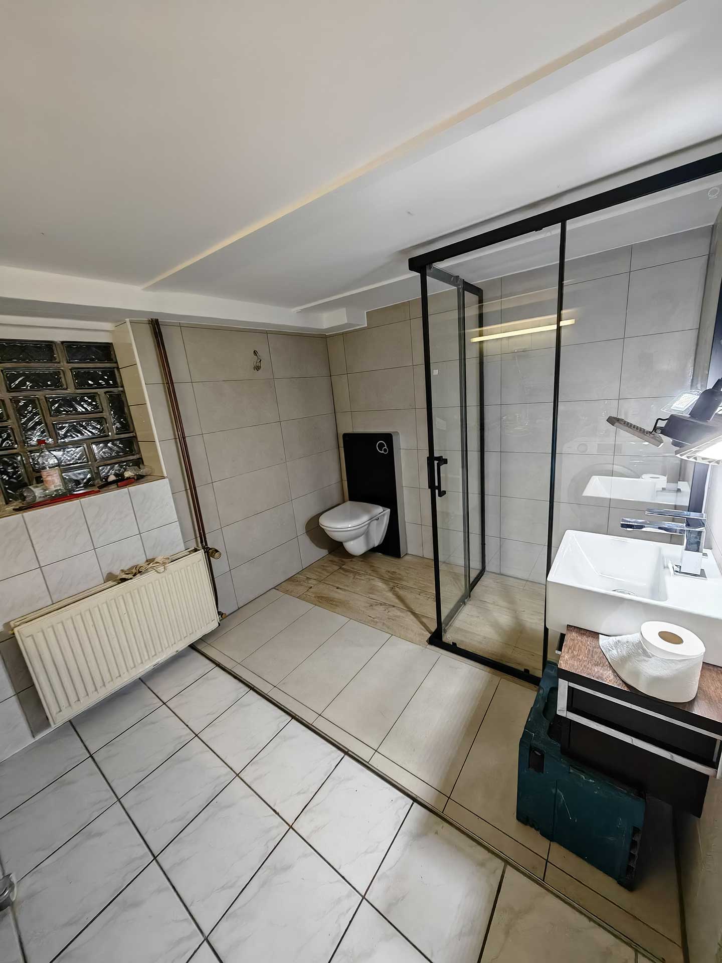 Sauberes Badezimmer mit weißer Keramik, Glastrennwand, Hänge-WC und Waschbecken.