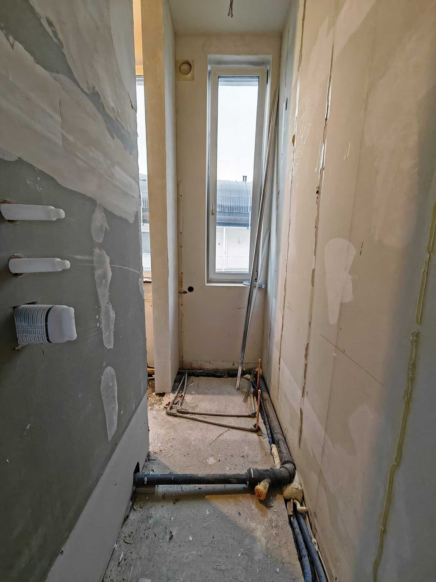 Unvollständiger Raum mit Rohren, unlackierten Wänden und einem hohen Fenster im Hintergrund.